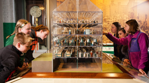 Students gather around a house shaped vitrine with miniatures inside