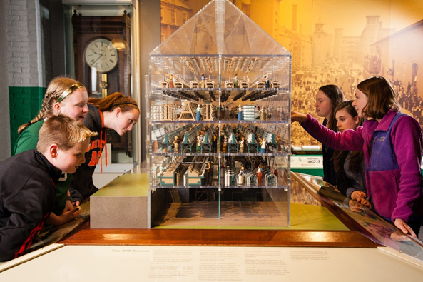 Students gather around a house shaped vitrine with miniatures inside