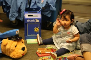 A very young child sits on the floor surrounded by accouterments.