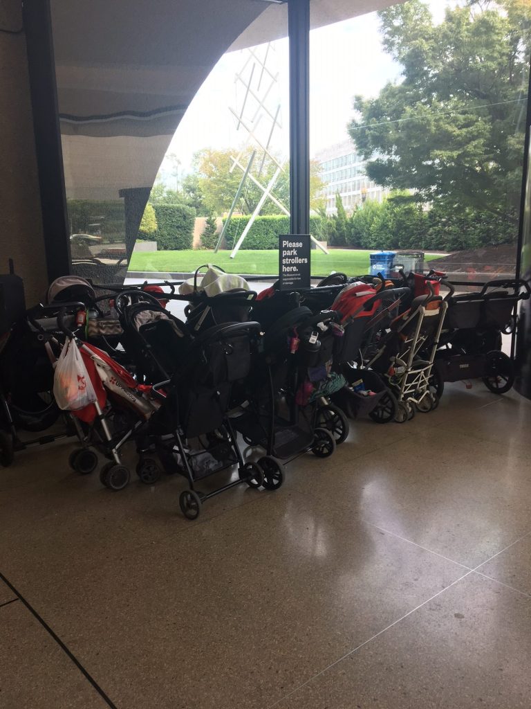 A group of strollers parked outside of an exhibition.