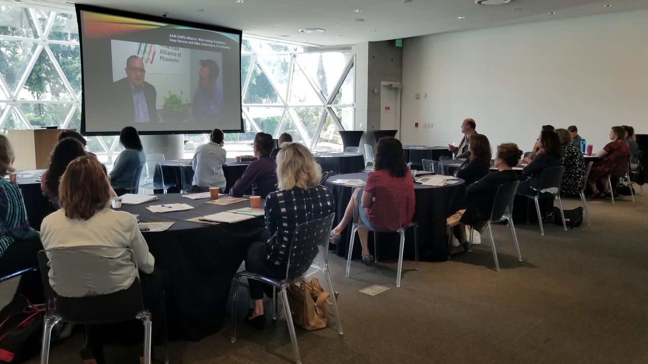 Image of a group of people seated at round tables at the Dali Museum's November 2017 AAM Convening on the LGBTQ Welcoming Guidelines. Participants are viewing a presentation on a screen at the front of the room.