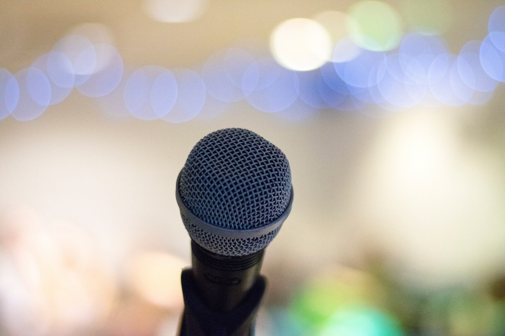 Image of a lone microphone with a blurred image of lights and people in the background.