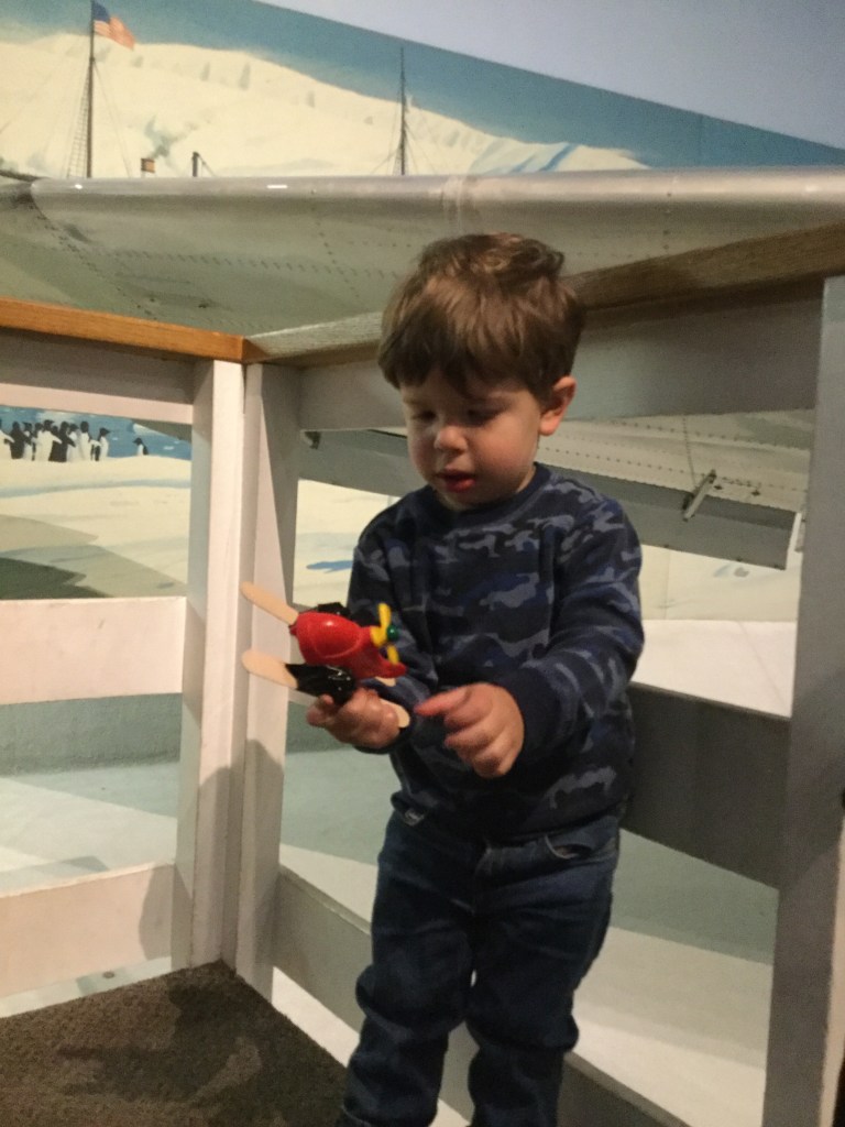 A little boy plays with a toy airplane in front of a real one.