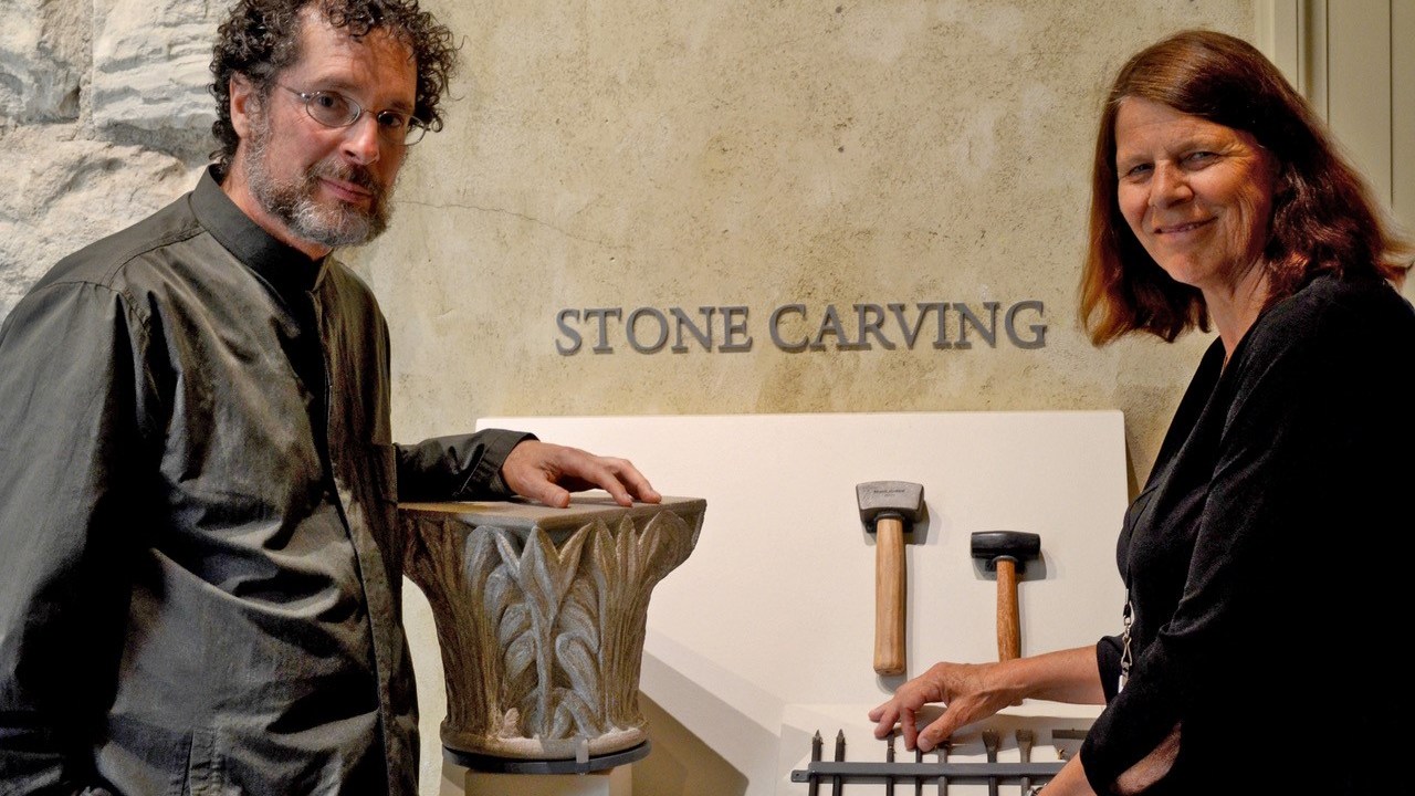 A man and a women standing together in front of a display with a column and stone carving tools