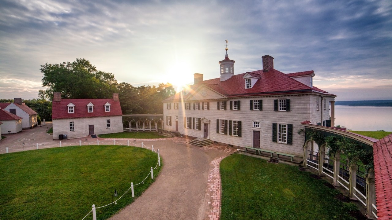 Image: Mt Vernon mansion at sunrise with the sun glinting off the roof and a green lawn stretching to the foreground