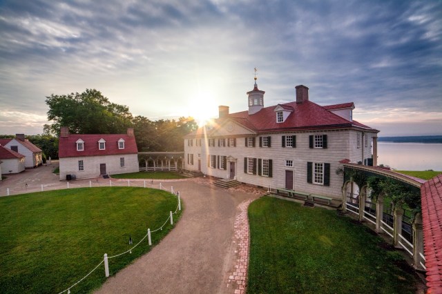 Image: Mt Vernon mansion at sunrise with the sun glinting off the roof and a green lawn stretching to the foreground