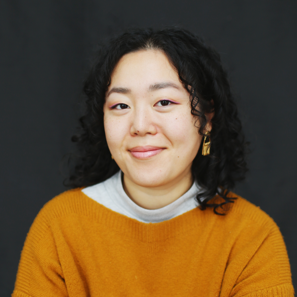 Gloria Roh with curly black hair and an orange sweater smiles.