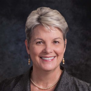 Headshot of a woman smiling at the camera with short grey hair and dangling earrings.