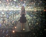 A woman stands in a Kusama installation and takes a selfie.