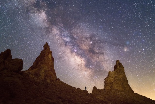 Image of the night sky with several sharp peaks in the foreground and a small person standing.