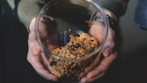 Image of a pair or hands holding a clear glass cookie jar with what look like oatmeal and raisin cookies inside. Shot taken from above looking down into the jar at an angle.
