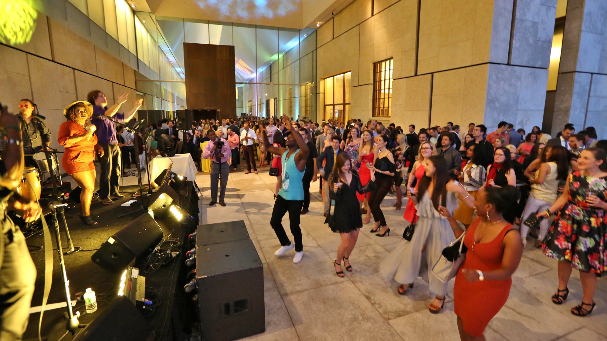 A group of young people are dancing in the atrium of the museum to music from the stage on the left of the image