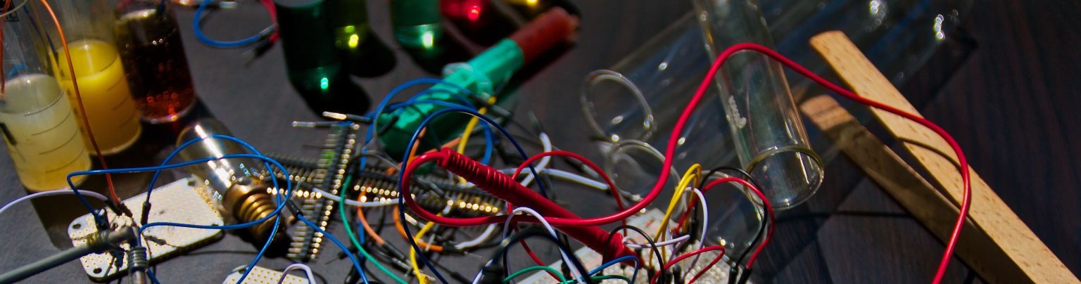 A circuit board with multi-colored wires and a multimeter on a black desktop