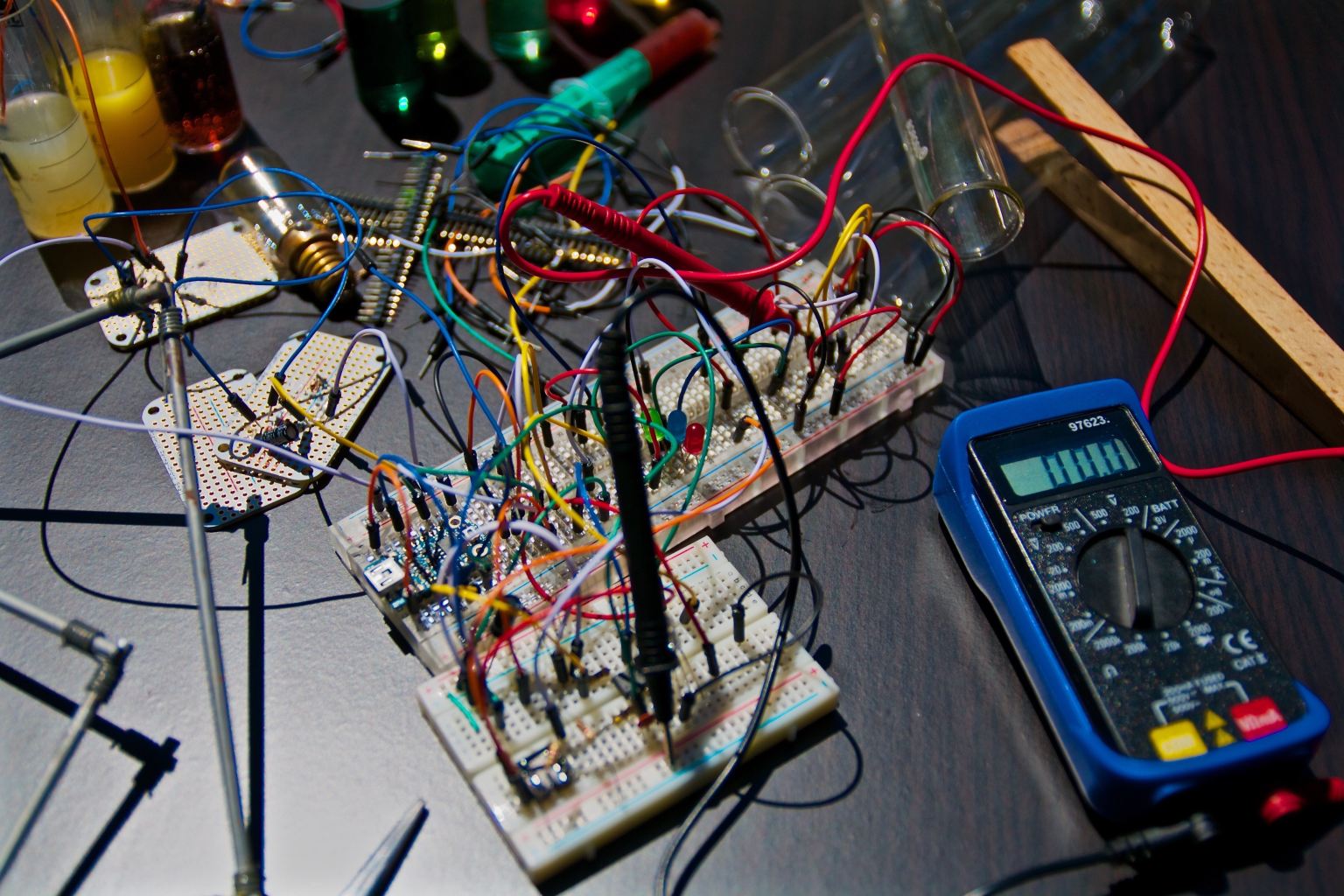 A circuit board with multi-colored wires and a multimeter on a black desktop
