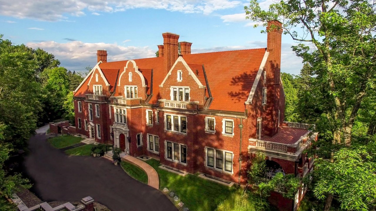 Image of the front of Glensheen house, a red brick Jacobean style mansion with a blacktop road and curved wheelchair ramp visible in front.