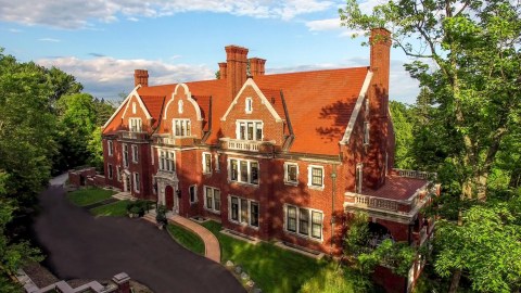 Image of the front of Glensheen house, a red brick Jacobean style mansion with a blacktop road and curved wheelchair ramp visible in front.
