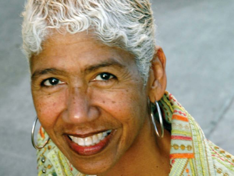 A headshot of Ericka Huggins wearing a green and orange patterned blouse