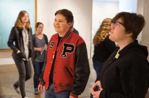 Two teenagers looking at art in the Warhol Museum galleries. One wears a red varsity letter jacket and the other wears a black sweatshirt