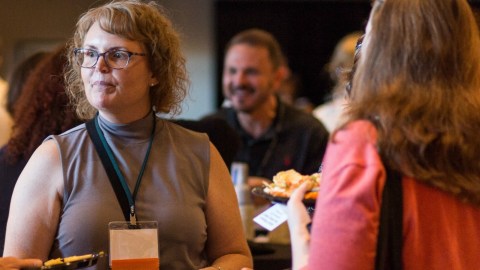 A woman stands with her name badge showing the blank backside in a crowd at a conference event.