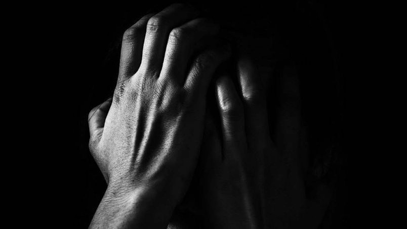 A person holds their hands to the face in black and white against a black backdrop.