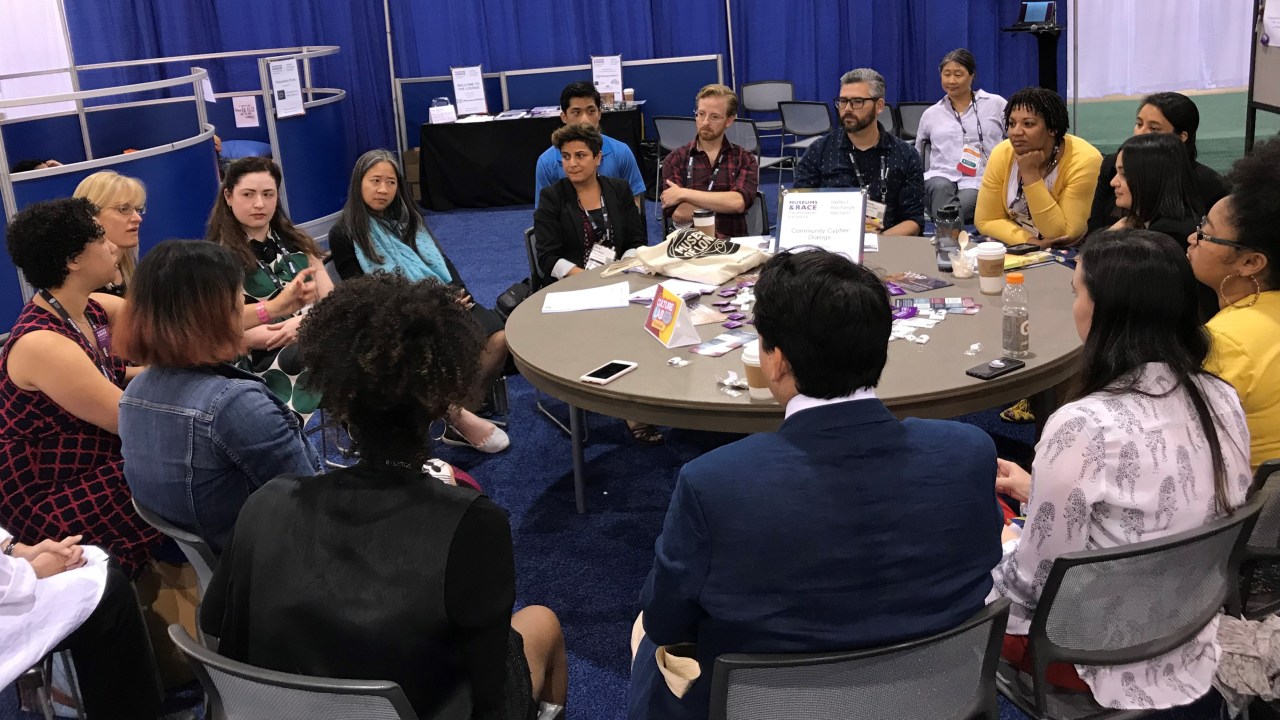 People sitting around a round table at the Museums and Race booth.