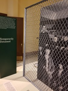 Image of an exhibit panel and installation at Ellis Island with the text panel that reads "Temporarily Detained"
