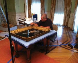 A man works on removing dust from a painting of George Washington. The painting is placed on a blanketed table.