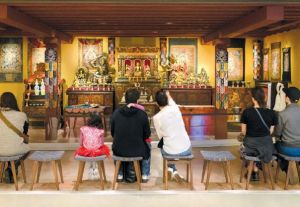 A group of people sit on stools in front of an Indian alter. 