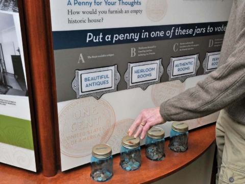 View of a text panel with four glass jars and someones hand touching the lid of one of the jars.