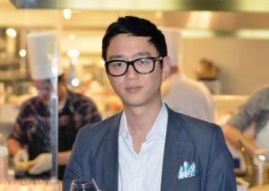 Headshot of Peter Kim with chefs seen blurred in the background. 