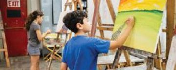 Two children (one female, one male) stand in front of easels painting.