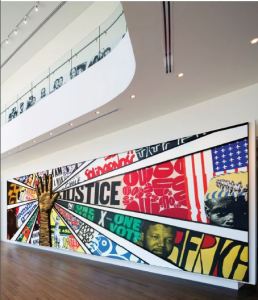 Image of a mural hanging on a wall with a giant raised hand and words and images radiating out from it. 