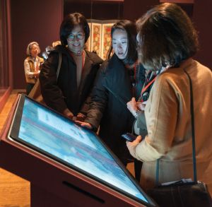Three women look down on an angled interactive screen. 