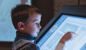 A young white boy touches an interactive screen. 