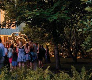 A group of people stand in a garden with drinks. 