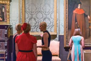 Four women stand in a group discussing a painting in a gallery. 