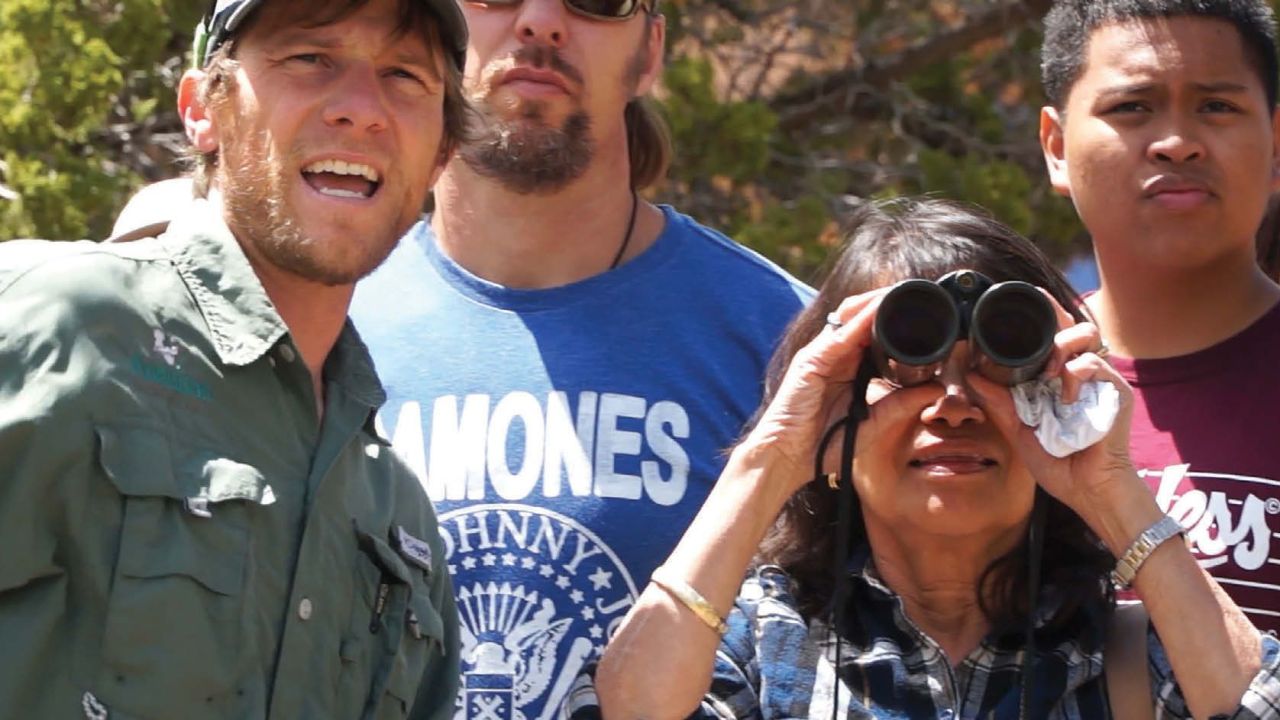 Three people look toward the camera, one, a woman holds a pair of binoculars.
