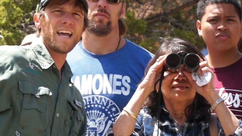Three people look toward the camera, one, a woman holds a pair of binoculars.