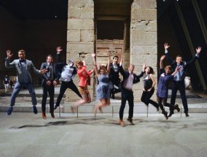 View of a group of Museum Hack personnel jumping with their hands in the air in front of an archaeological artifact inside a museum. 