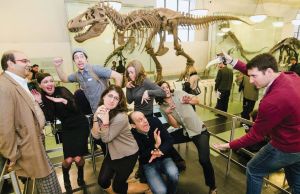 A group of Museum Hack staff standing on a platform in front of a Tyrannosaurus Rex skeleton. 