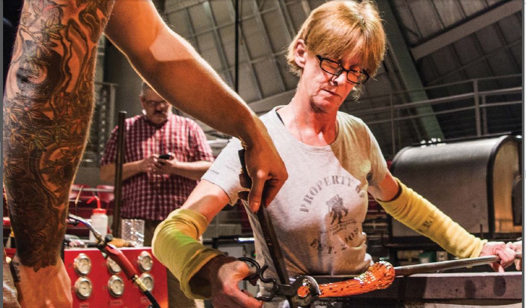 A woman works a piece of glass on a metal tube.