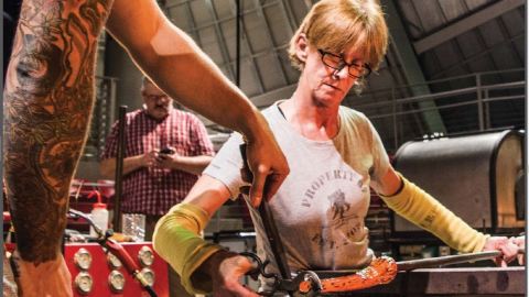 A woman works a piece of glass on a metal tube.