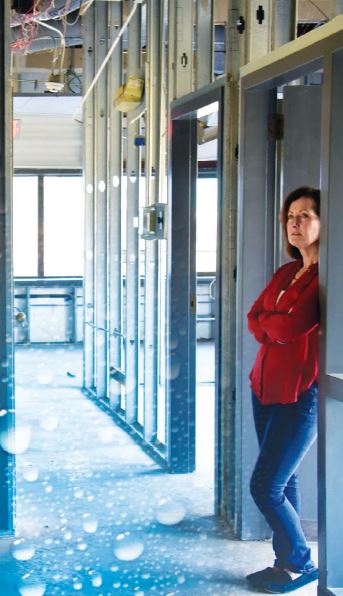 A woman stands in the doorway to a with her arms crossed surveying water damage to her museum.