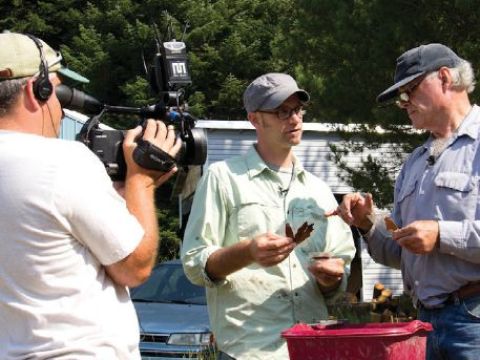 Image of three men discussing a leaf while on camera (one of the men is a cameraman). 