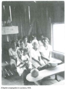 Black and white image of several African American women sitting on benches in a wooden structure.