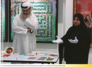 A man wearing a white long shirt and headdress and a woman wearing a black burka stand by a table explaining the right way to handle an object. 