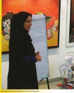 A woman in a black burka stands beside a flipboard sitting in front of a painting. 