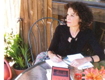 Julia Alvarez sitting in a chair outside with a notebook in front of her. 
