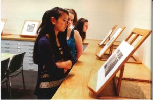 Several young women look at sketches displayed on top of map drawers on small easels. 