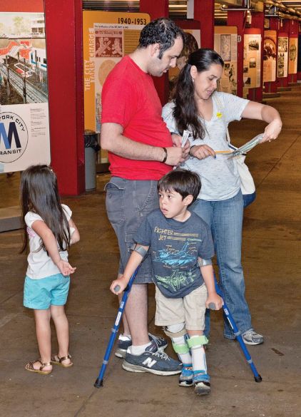 A family stands reading a map in a gallery with two small children, one has leg braces and crutches. 